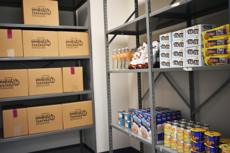 Image shows various packaged goods and Helping Harvest boxes lining the shelves of the Tamaqua Center food pantry.